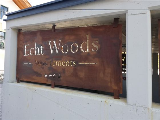 Das Bild zeigt ein Schild mit der Aufschrift "Echt Woods" und dem Wort "Announcements". Das Schild ist aus Metall und wirkt rustikal.