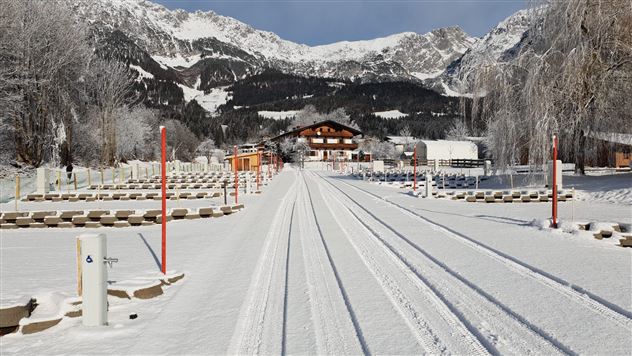 Eine verschneite Landschaft mit Schienen, die in die Berge führen. Im Hintergrund ist ein traditionelles Gebäude und Bäume zu sehen.