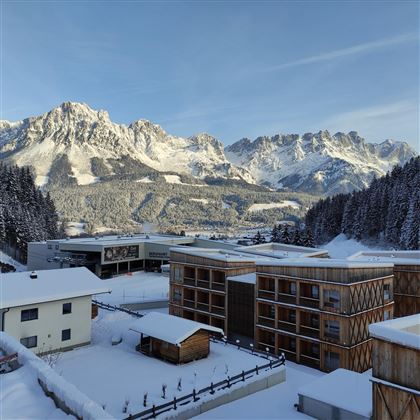 A winter landscape with snow-covered mountains and modern buildings. The surroundings are quiet and picturesque, surrounded by spruce forest.
