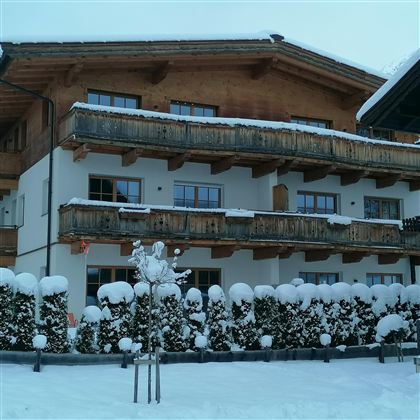 Ein Gebäude im Schnee mit einem Holzbalkon. Der Garten ist mit schneebedeckten Sträuchern dekoriert.