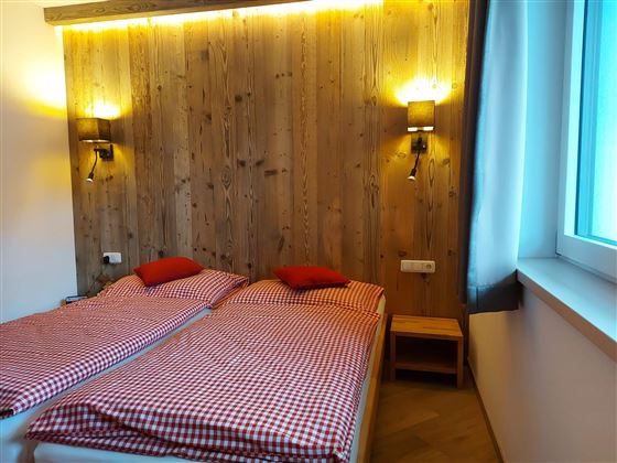 A cozy room with two single beds and checked bedding. The walls are made of wood and there is soft lighting.