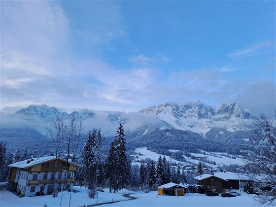 A wintry landscape with snow-covered mountains and scattered houses. The sky is cloudy, giving the scene a tranquil mood.