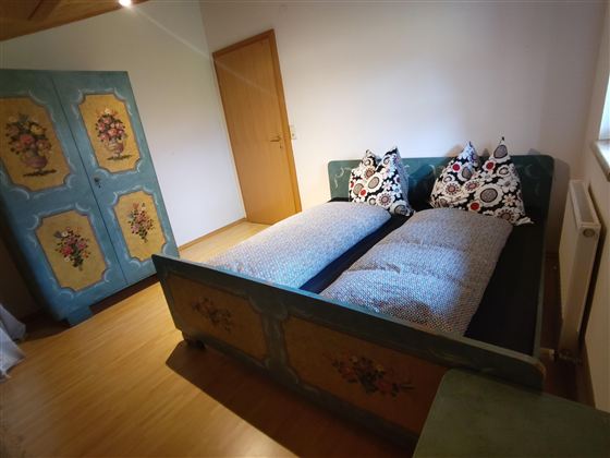 Een gezellige slaapkamer met een tweepersoonsbed en kleurrijke kussens. Naast het bed staat een decoratieve kast in traditionele stijl.