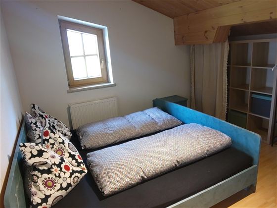 Een gezellige kamer met twee bedden en kleurrijke kussens. Een raam laat veel daglicht binnen.