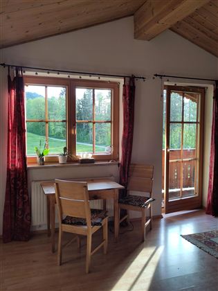 Een gezellige kamer met een tafel en twee stoelen. Door de ramen kijk je de natuur in en het daglicht stroomt naar binnen.