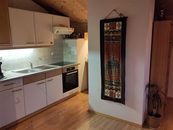 Een moderne keuken met witte kasten, een fornuis en een gootsteen. Aan de muur hangt een kleurrijk wandtapijt.