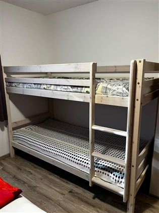 A bunk bed made of wood with an upper and a lower mattress. The room has a simple and modern style with a wooden floor.