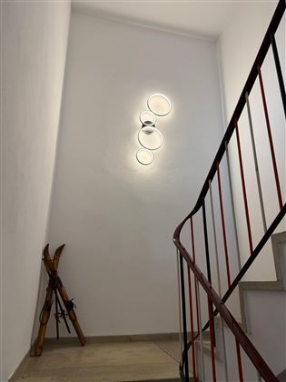 Ein heller Treppenaufgang mit modernen Wandlichtern. In der Ecke steht ein Paar Skier.