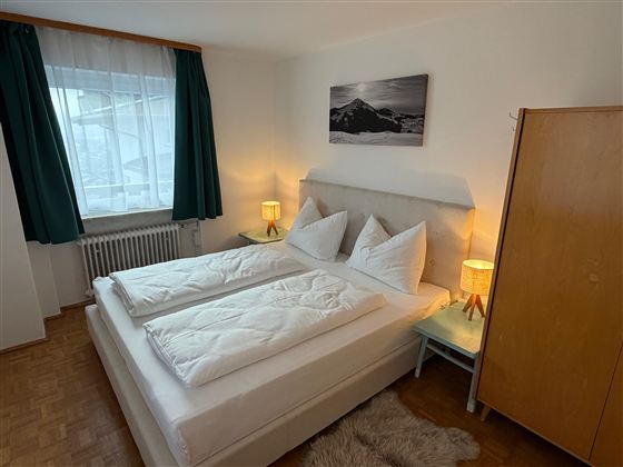 Ein gemütliches Schlafzimmer mit einem Doppelbett und zwei Nachttischen. Der Raum hat große Fenster und einen modernen Kleiderschrank.