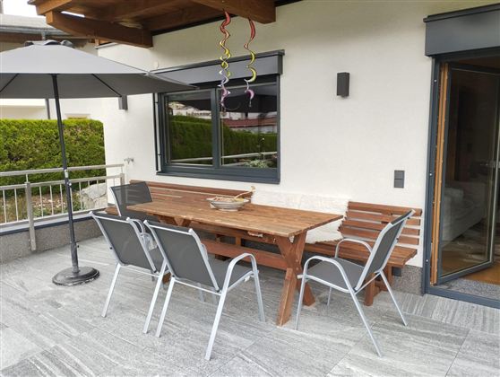 An inviting outdoor area with a wooden table and chairs. A sunshade protects against direct sunlight.