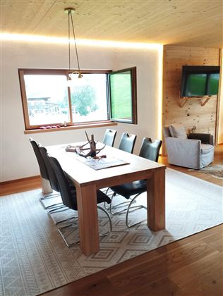 A modern dining room with a wooden table and black chairs. Large windows offer a view of the landscape.