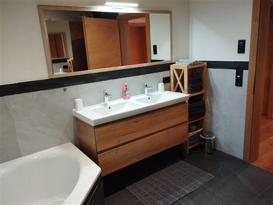 A modern bathroom with a double sink made of wood and elegant fixtures. The walls are light and the floor is made of dark tiles.