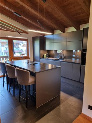Modern kitchen with dark furniture and a large kitchen island. Large windows let in plenty of daylight and offer a view outside.
