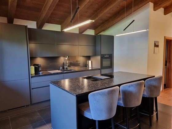 Modern kitchen with a large kitchen island and stylish bar stools. The room has a bright and open atmosphere with wooden ceilings and modern surfaces.
