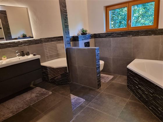 A modern bathroom with an elegant bathtub and a stylish sink. Large windows let in plenty of daylight and offer a view of the green surroundings.