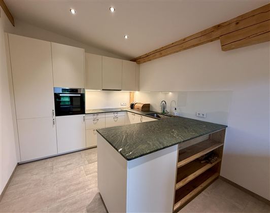 Eine moderne Küche mit hellen Schränken und einer eleganten Arbeitsfläche aus Stein. Der Raum hat eine offene und geräumige Atmosphäre.
