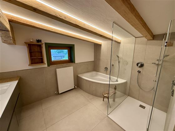Ein modernes Badezimmer mit einer Dusche und einer Badewanne. Die Holzdetails und das Fenster sorgen für eine gemütliche Atmosphäre.