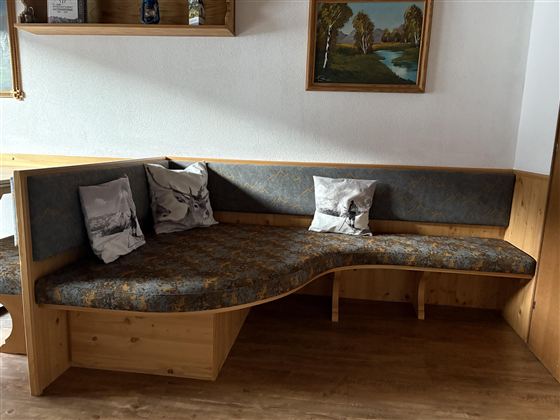 A cozy wooden seating area with a curved bench. A few cushions and a painting enhance the atmosphere of the room.