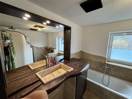 Ein modernes Badezimmer mit einem stilvollen Holzwaschtisch und zwei Waschbecken. Im Hintergrund ist eine Badewanne und ein Fenster mit Blick ins Freie.