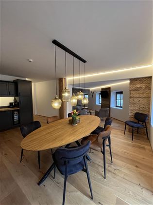 Moderní jídelna s oválným dřevěným stolem a elegantními židlemi. Osvětlení prostoru tvoří stylové závěsné lampy a vytváří útulnou atmosféru.