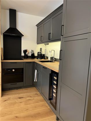 Moderní kuchyň s šedými skříňkami a dřevěnou pracovní deskou. Je dobře vybavená kuchyňskými spotřebiči a nabízí dostatek úložného prostoru.