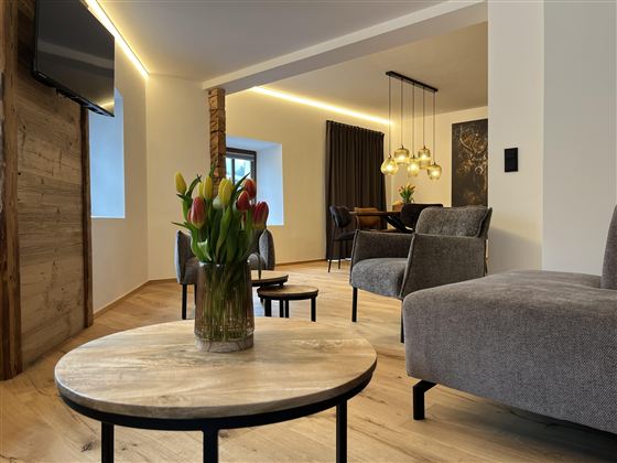 Moderně zařízený prostor s dřevěnou podlahou a útulným sezením. Na stole stojí váza s čerstvými tulipány.