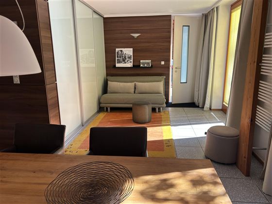 Een moderne interieur met lichte muren en houten accenten. Een eettafel, een bank en een comfortabele stoel zijn zichtbaar.