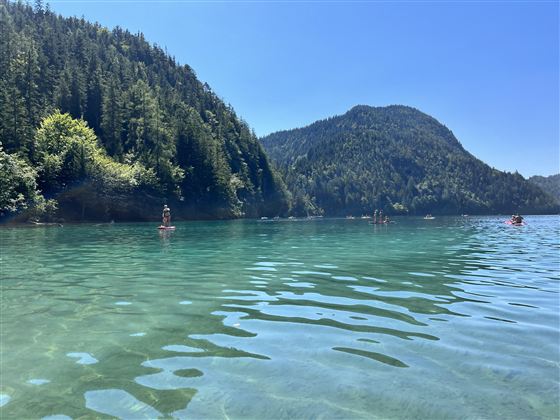Een heldere meer omgeven door groene bossen en bergen. Mensen genieten van de rust van het water op een zonnige dag.