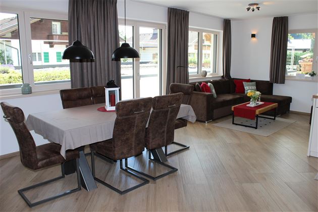 A modern and inviting living kitchen with a dining table and comfortable seating. Large windows let in plenty of daylight and create a bright atmosphere.