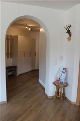 A bright entrance area with an arched passage. On the right side, there is a small table with brochures and on the left are white cabinets.