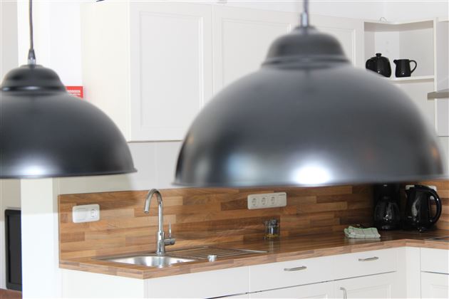 A modern kitchen with wood details and elegant black pendant lights. In the background, dishes and appliances are visible.