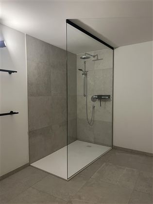 Moderní sprcha s proskleným oddělením a elegantními dlaždicemi. Prostor působí světlým a prostorným dojmem.