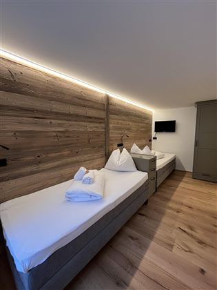 Moderní ložnice se dvěma samostatnými postelemi a teplými dřevěnými tóny. Jemné osvětlení vytváří útulnou atmosféru.