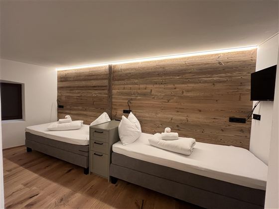 Pohodlná ložnice se dvěma jednolůžkovými postelemi a moderním dřevěným designem. Teplá světla vytvářejí vítanou atmosféru.