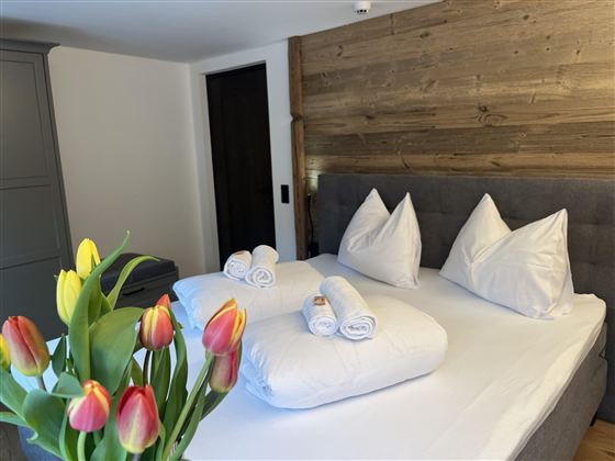 Pohodlná ložnice s velkou postelí a čerstvými ručníky. Na nočním stolku je kytice barevných tulipánů.