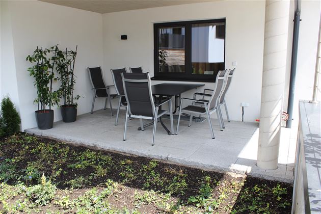 An inviting patio with a table and six chairs. In the background, there are some plants, and there is plenty of daylight.