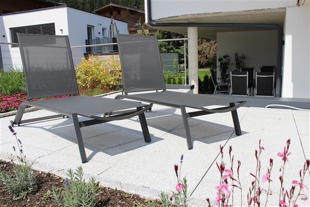 Two modern loungers on a terrace. In the background, plants and a cozy seating area are visible.