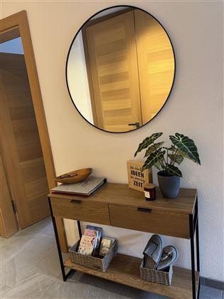 Een moderne entree met een ronde spiegel en een stijlvolle console tafel. Op de tafel staan planten en enkele gedecoreerde objecten.