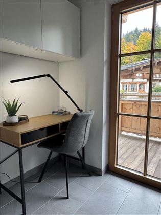 Een moderne werkruimte met een houten bureau en een ergonomische stoel. Door het raam is er een mooi uitzicht op de buitenkant met bomen en een terras.