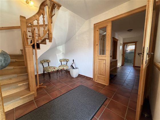 Ein einladender Flur mit einer Holztreppe und gemütlichem Mobiliar. Ein großer Teppich und fliesenboden verleihen dem Raum Wärme und Komfort.