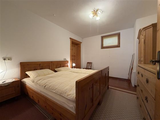 Ein gemütliches Schlafzimmer mit einem großen Holzbett und zwei Kissen. Die Wände sind hell, und es gibt einen Schrank sowie eine kleine Nachtkommode.