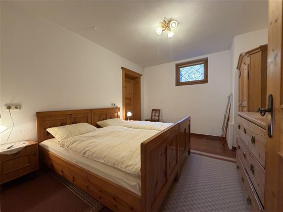 Ein gemütliches Schlafzimmer mit zwei Einzelbetten aus Holz. Die Wände sind hell und es gibt einen kleinen Fensterbereich mit natürlichem Licht.