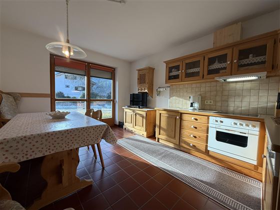 Eine helle Küche mit Holzschränken und einem großen Tisch. Ein Fenster bietet Aussicht auf den Garten.