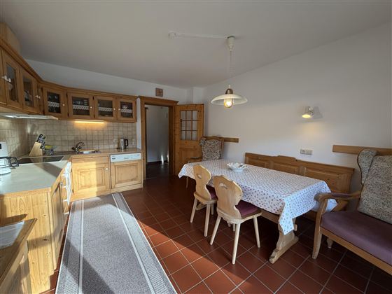 Eine gemütliche Küche mit Holzregalen und einem Esstisch. Die Einrichtung ist einfach und einladend mit ausreichend Platz zum Kochen und Essen.