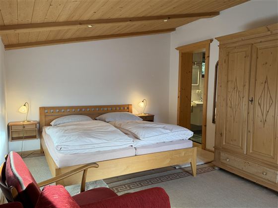 Ein gemütliches Schlafzimmer mit einem großen Bett, zwei Nachttischen und einem roten Sofa. Die Wände sind hell, und es gibt einen rustikalen Kleiderschrank aus Holz.