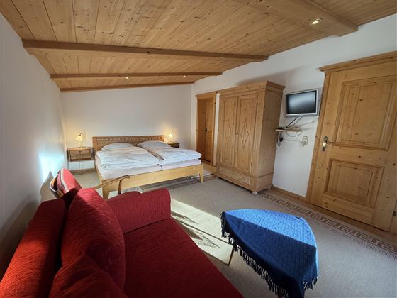 Ein gemütliches Schlafzimmer mit einem Doppelbett und einem roten Sofa. Der Raum hat Holzmöbel und einen Fernseher an der Wand.