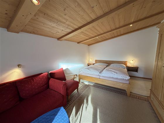 Ein gemütliches Schlafzimmer mit einem Doppelbett und einem roten Sofa. Das Holzdecken und die sanfte Beleuchtung sorgen für eine einladende Atmosphäre.