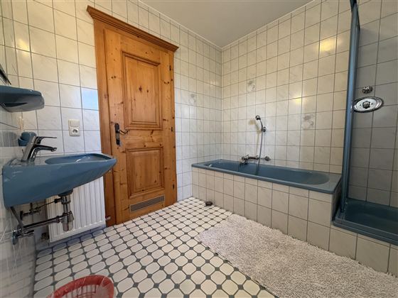 Ein Badezimmer mit weißen Fliesen und blauen Sanitäranlagen. Es gibt eine Badewanne, eine Dusche und eine Holz-Tür.