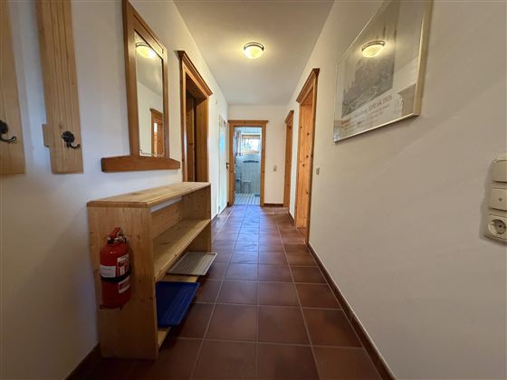 Ein heller Flur mit Holzverkleidungen und Spiegeln. Auf der linken Seite steht ein Schuhregal und an der Wand hängt ein Feuerlöscher.