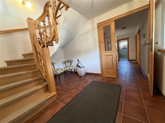 Ein einladender Flur mit einer Holztreppe und Fliesenboden. Auf der linken Seite befinden sich einige Stühle und eine Tür, die zu weiteren Räumen führt.